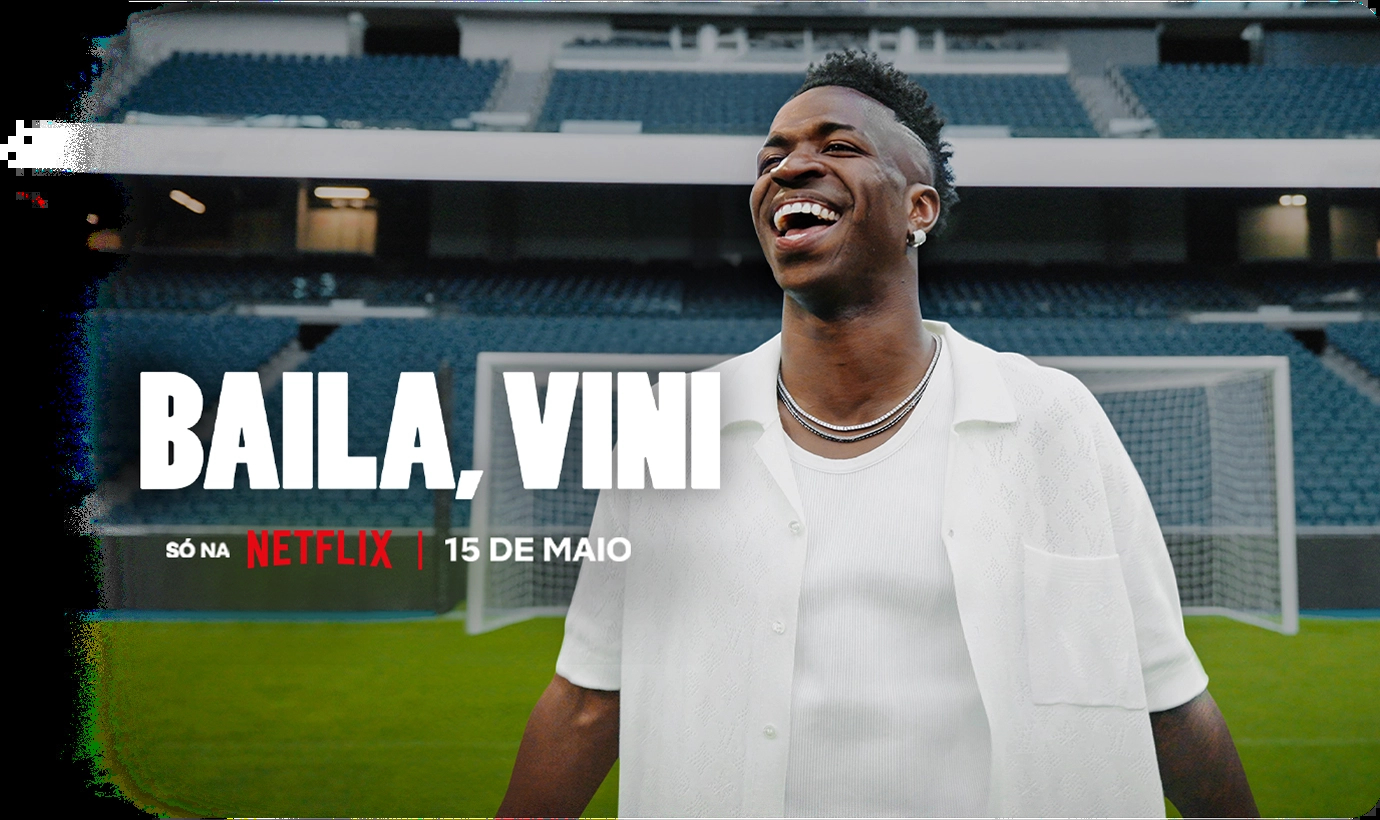 Fundo preto com o texto “Round 6 - Temporada 2” com texto abaixo: “Só na Netflix | Já disponível”. À direita, personagem vestindo um moletom vermelho com capuz e uma máscara preta com um circulo grande no centro.