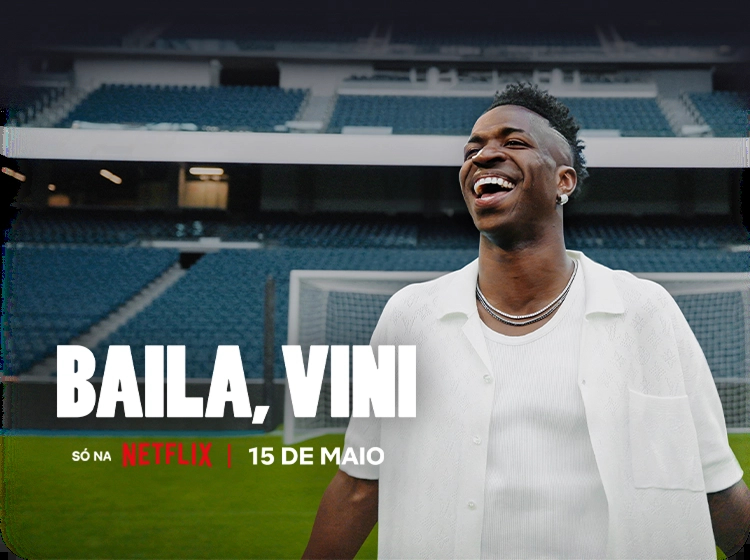 Fundo preto com o texto “Round 6 - Temporada 2” com texto abaixo: “Só na Netflix | Já disponível”. À direita, personagem vestindo um moletom vermelho com capuz e uma máscara preta com um circulo grande no centro.