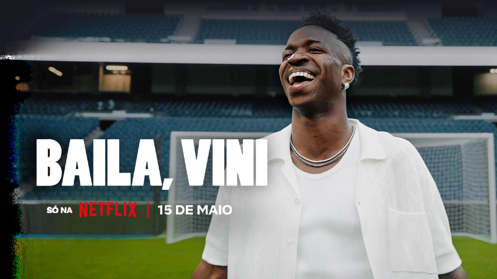 Fundo preto com o texto “Round 6 - Temporada 2” com texto abaixo: “Só na Netflix | Já disponível”. À direita, personagem vestindo um moletom vermelho com capuz e uma máscara preta com um circulo grande no centro.