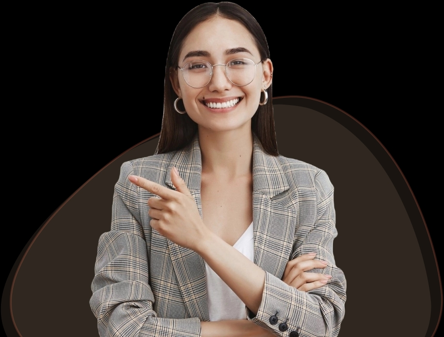 Uma mulher jovem com cabelo longo e liso usa óculos de armação transparente. Ela está vestindo uma jaqueta xadrez cinza sobre uma camiseta branca e jeans. Ela sorri calorosamente e aponta para o canto superior direito com a mão direita, enquanto mantém o braço esquerdo cruzado. Sua expressão é alegre e acolhedora.