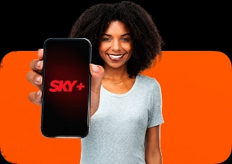 Mulher negra segura um smartphone em primeiro plano, exibindo a tela com o logotipo da SKY+. Uma forma quadrada com cantos arredondados está posicionada atrás dela.