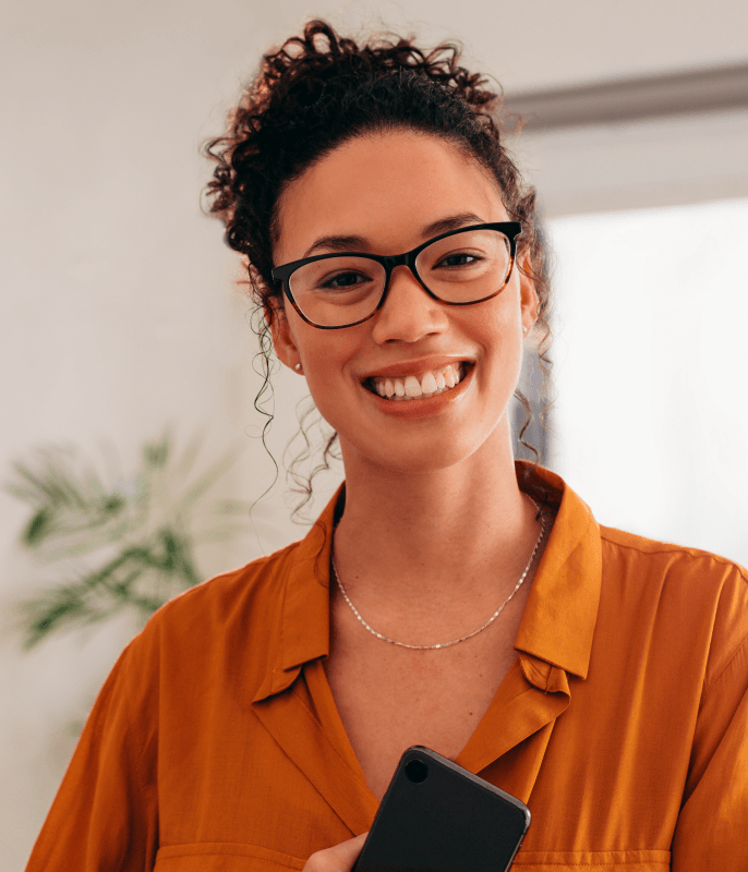 Mulher sorridente usando óculos e segurando um celular.
