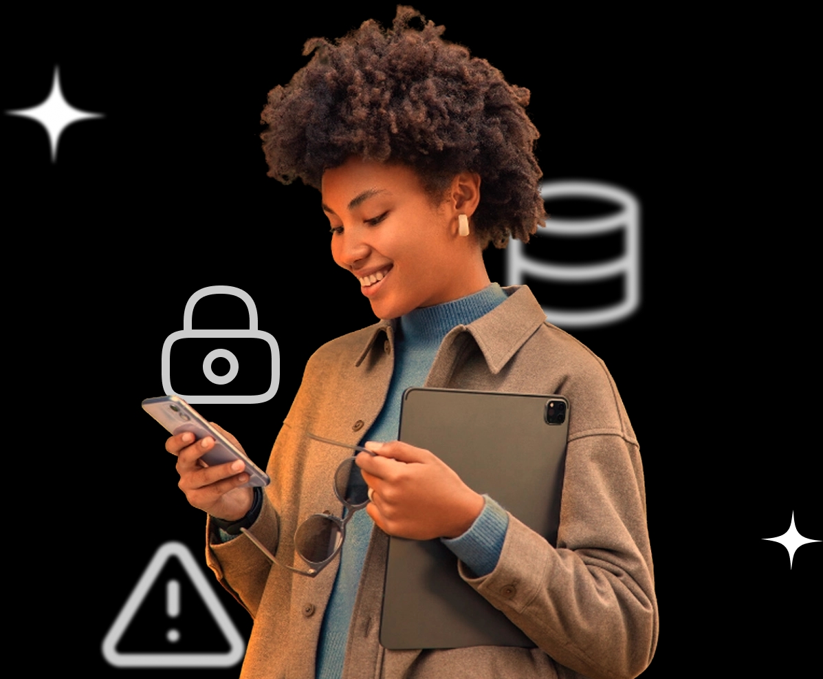 Uma mulher com cabelo curto e crespo segura um celular na mão esquerda e um tablet escuro na mão direita. Ela está olhando para o celular. Ícones de cadeado, uma base de dados e um triângulo de aviso estão ao redor.