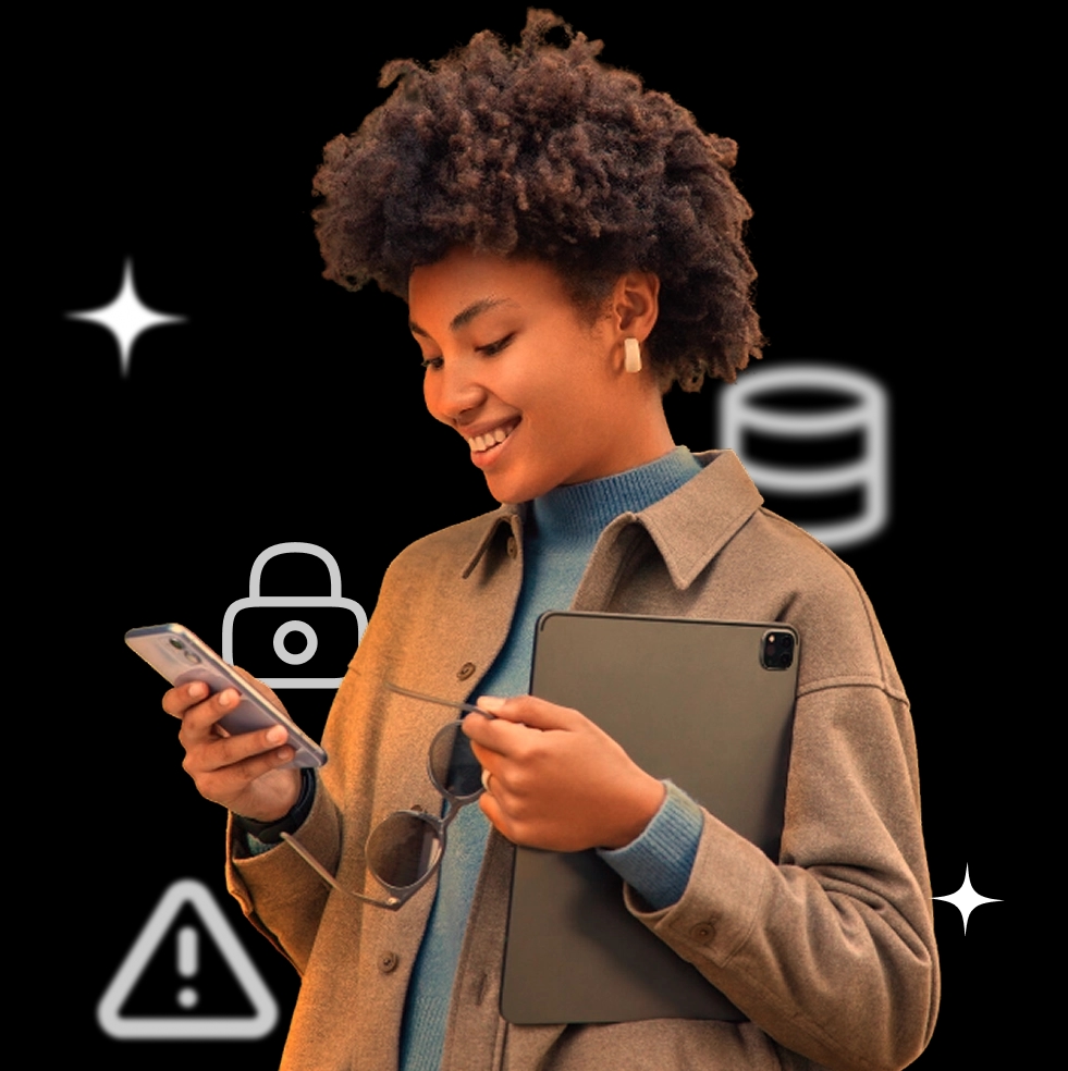 Uma mulher com cabelo curto e crespo segura um celular na mão esquerda e um tablet escuro na mão direita. Ela está olhando para o celular. Ícones de cadeado, uma base de dados e um triângulo de aviso estão ao redor.